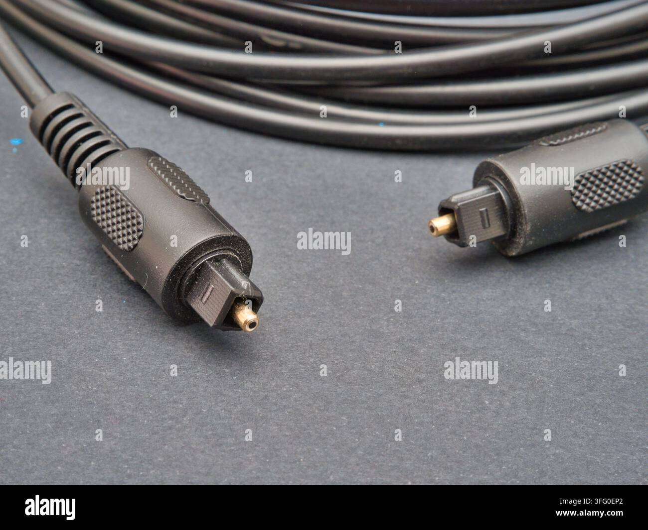 Schwarzes optisches Audiokabel – Ein schwarzes optisches Audiokabel mit TOSLINK-Steckern, ordentlich aufgerollt auf einem dunkelgrauen Hintergrund, bereit für High-Fidelity-Digi Stockfoto