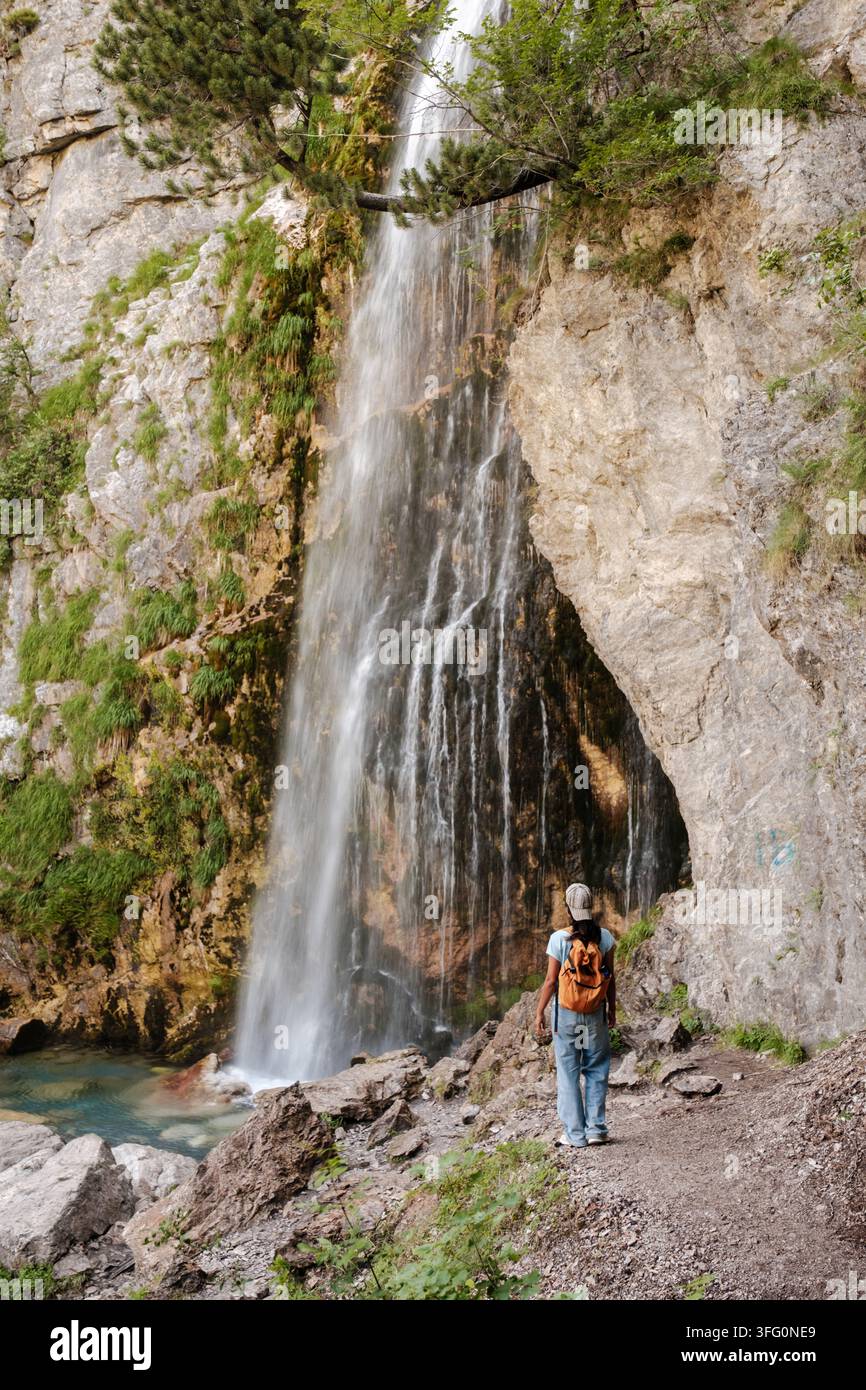 Ein Reisender steht ehrfürchtig am Fuße eines prächtigen Wasserfalls in Teth, Albanien. Stockfoto