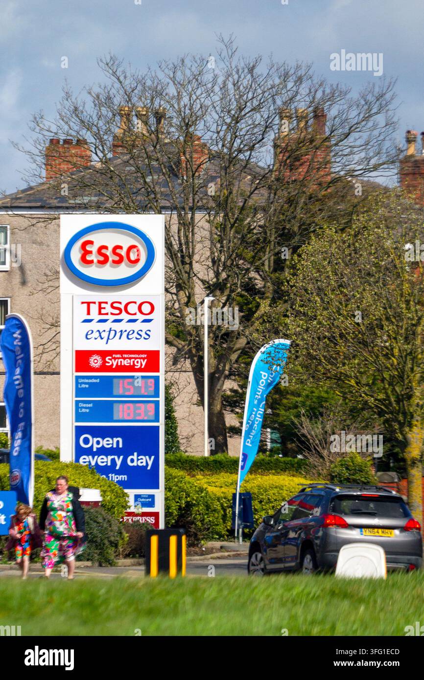 An einer Esso-Tankstelle mit einem Tesco Express zeigt ein Preistotem die Kraftstoffpreise, während ein Auto vorbeifährt. Southport, UK. Stockfoto