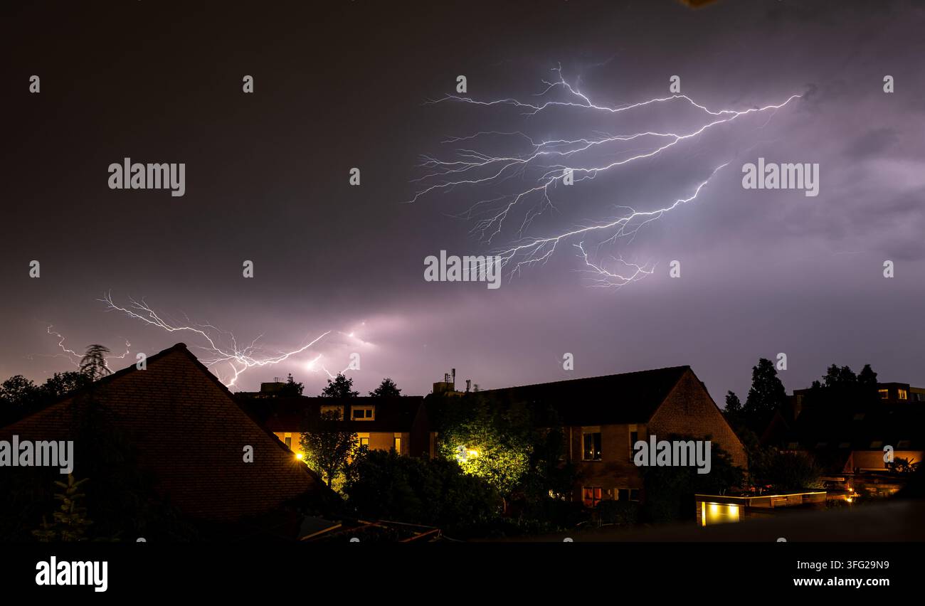 Dramatisches Spinnenblitz über einer Wohngegend bei Nacht, der Wolken und Häuser beleuchtet. Stockfoto