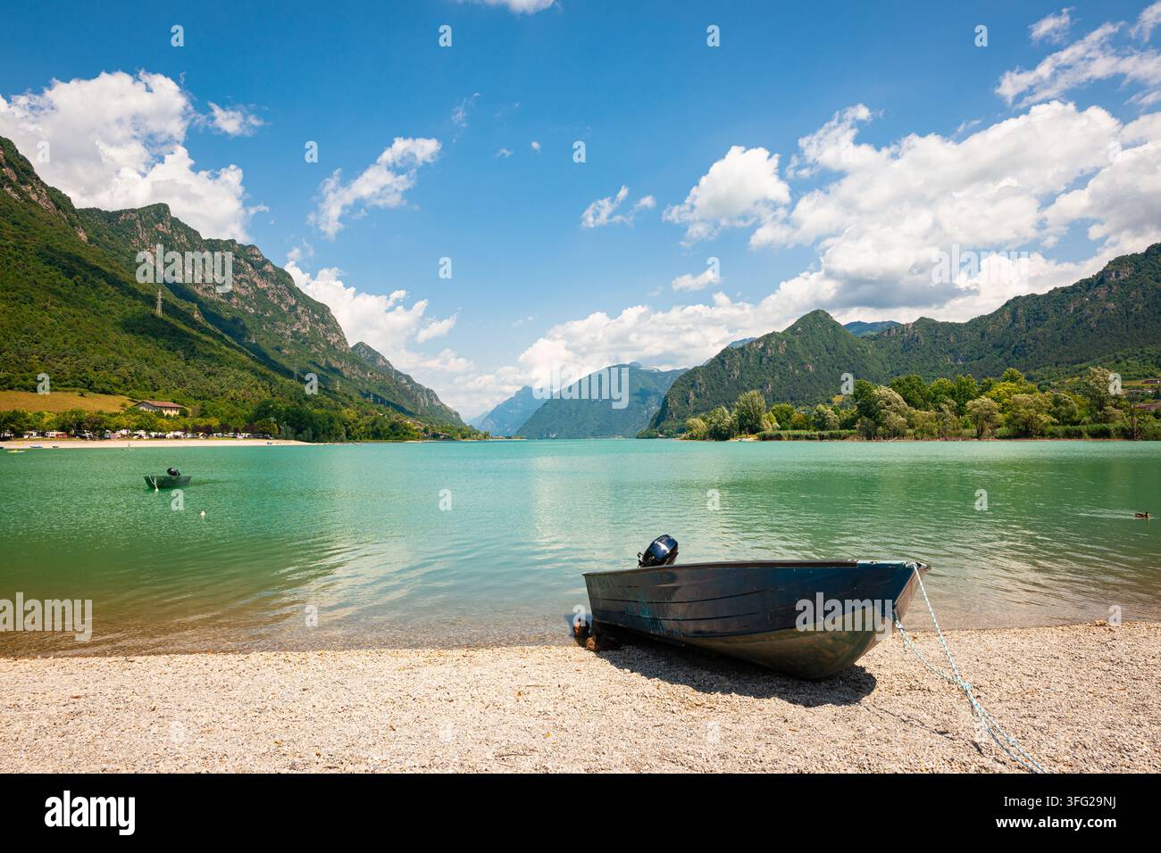 Kleines Ruderboot am Ufer eines Bergsees mit Bergen, blauem Himmel und Kiesstrand. Stockfoto
