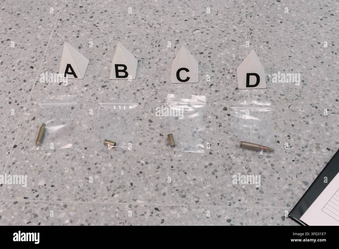 Vier transparente Beweismittelbeutel mit Patronenhülsen und einer Patrone sind auf dem Boden unter den Tatortmarkierungen A, B, C und D angeordnet. Stockfoto