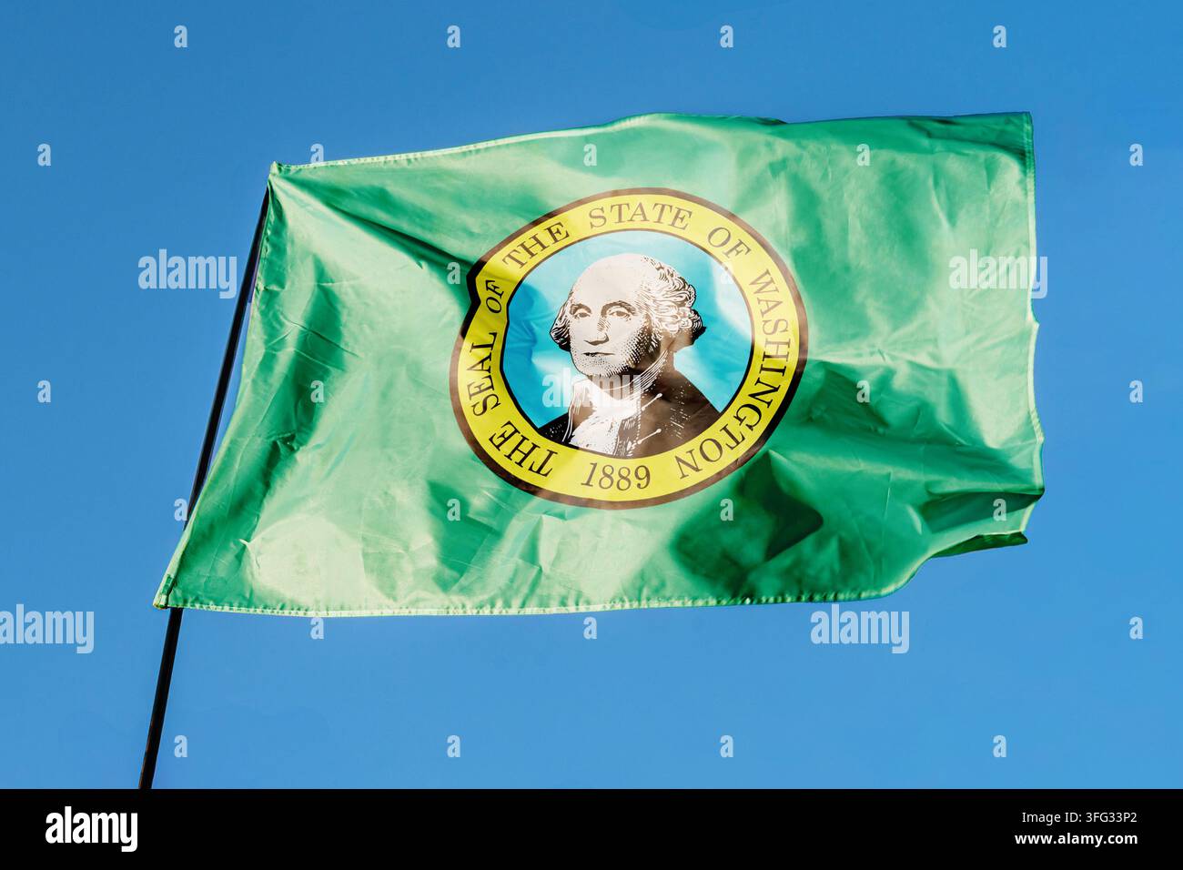 Flagge von Washington. Fahne weht im Wind vor einem klaren blauen Himmel, flatternd an einem Flaggenmast im Freien. Heller Sonnentag, Stofftextur, Außengewächs Stockfoto