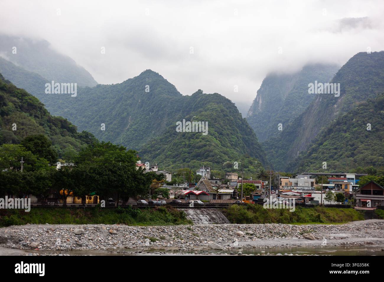 Neblig grüne Berge mit Blick auf das Dorf Sanzhanxi in Hualien, Taiwan. Felsenbett und üppige Vegetation unter einem bewölkten Himmel. Stockfoto