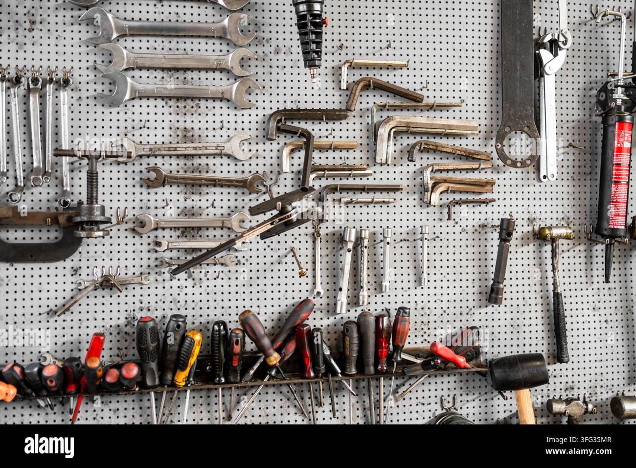 Organisierte Sammlung von Handwerkzeugen, darunter Schraubenschlüssel, Schraubendreher, Inbusschlüssel und Hämmer, die an einer Stecktafel in einer Werkstatt hängen. Stockfoto