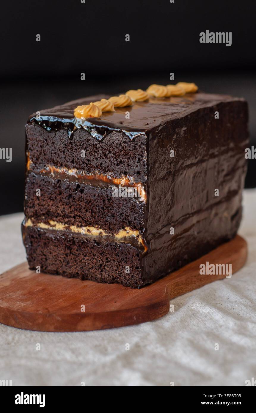 Reicher Schokoladen-London-Kuchen, geschichtet mit Karamell und überzogen mit glänzender Ganache, garniert mit gekniffeltem Zuckerguss Stockfoto