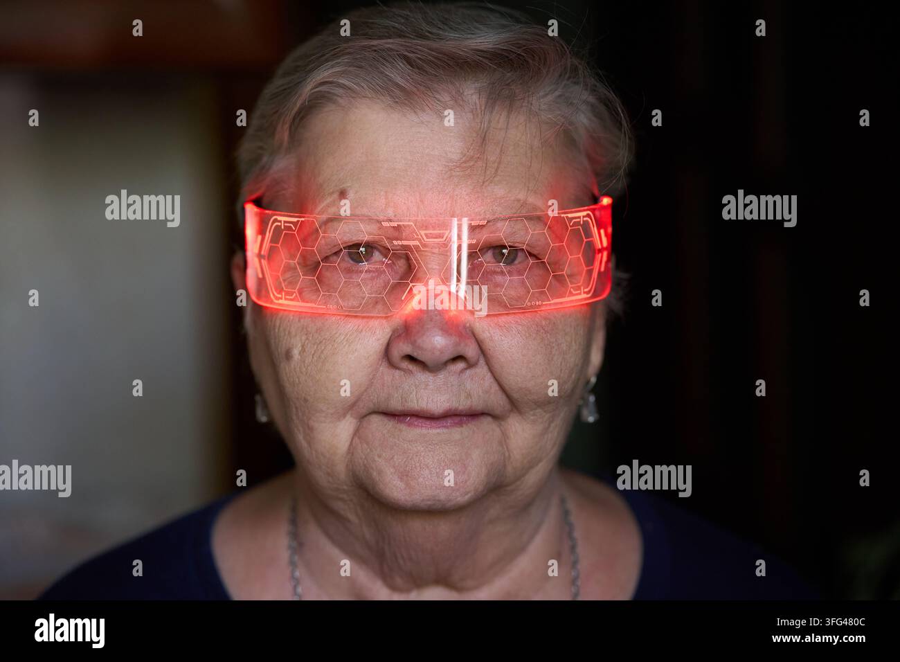 Eine ältere Frau trägt hell beleuchtete, futuristische Brillen, was einen auffälligen visuellen Effekt erzeugt. Geeignet für Tech-, Innovations- oder Lifestyle-Themen Stockfoto