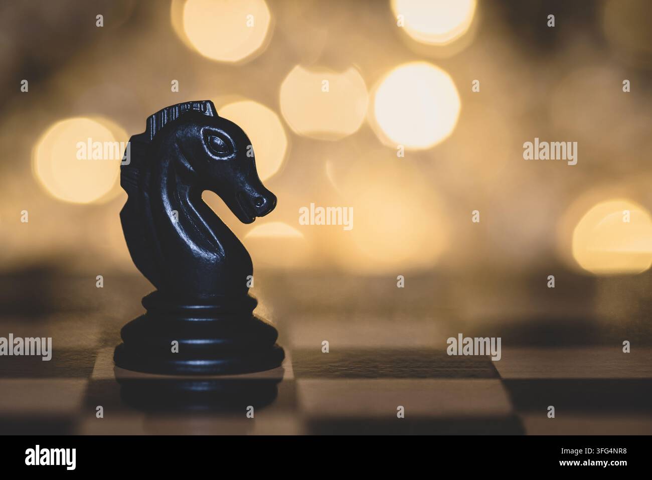 Einziger schwarzer Schachspringer steht auf einem Schachbrett mit einem warmen, leuchtenden goldenen Bokeh-Hintergrund, der Strategie und Führung symbolisiert. Stockfoto