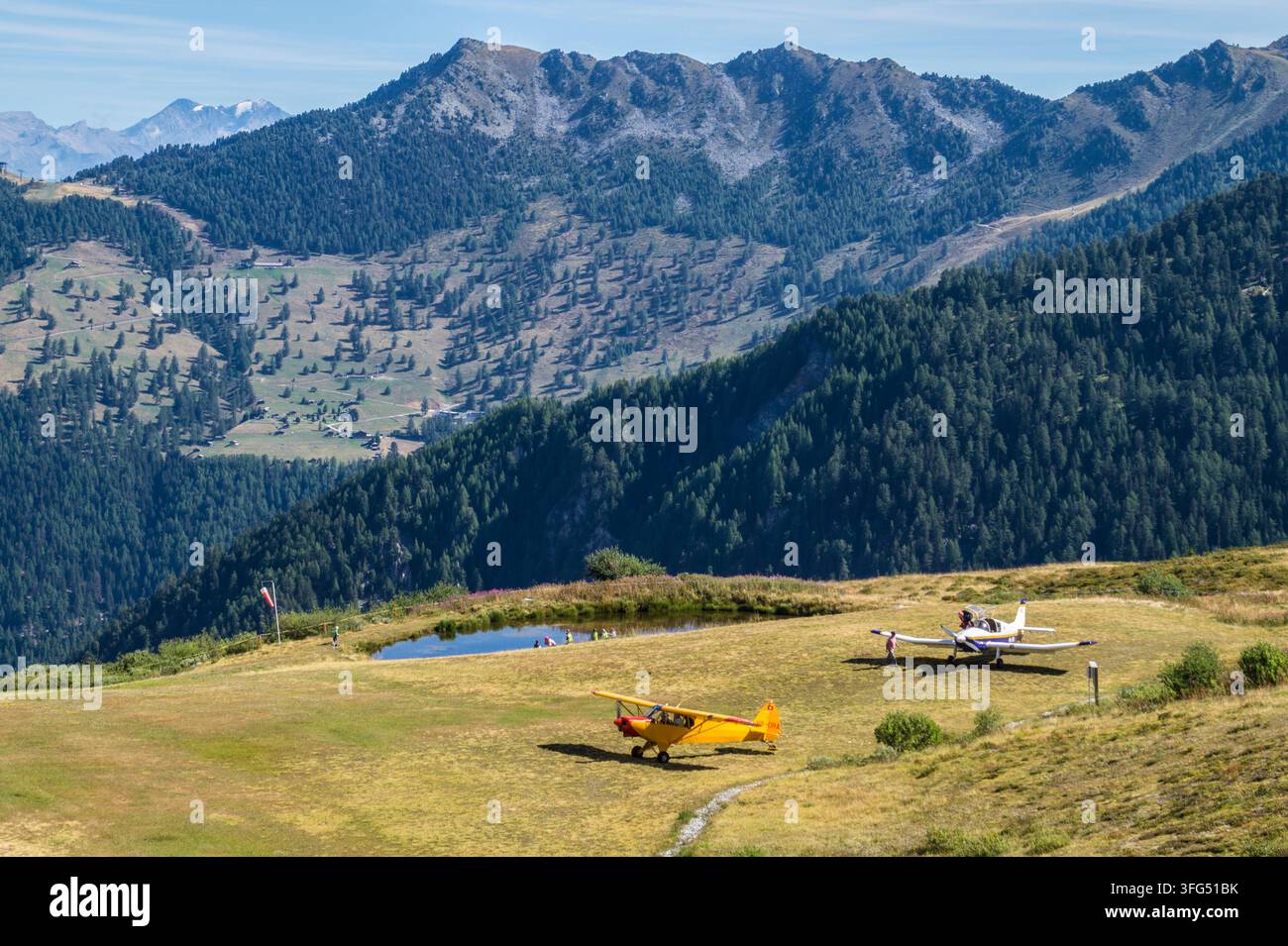 Zwei kleine Flugzeuge, die auf einer grasbewachsenen Fläche in der Nähe von Bergen geparkt sind Stockfoto