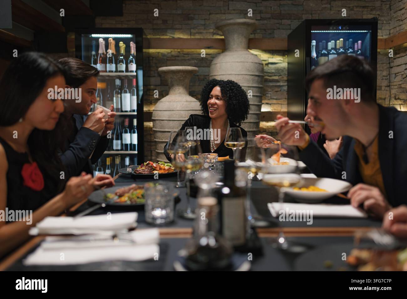 Eine Gruppe vielfältiger Freunde genießt Essen und Getränke und führt lebhafte Gespräche in einem Restaurant am Abend. Stockfoto