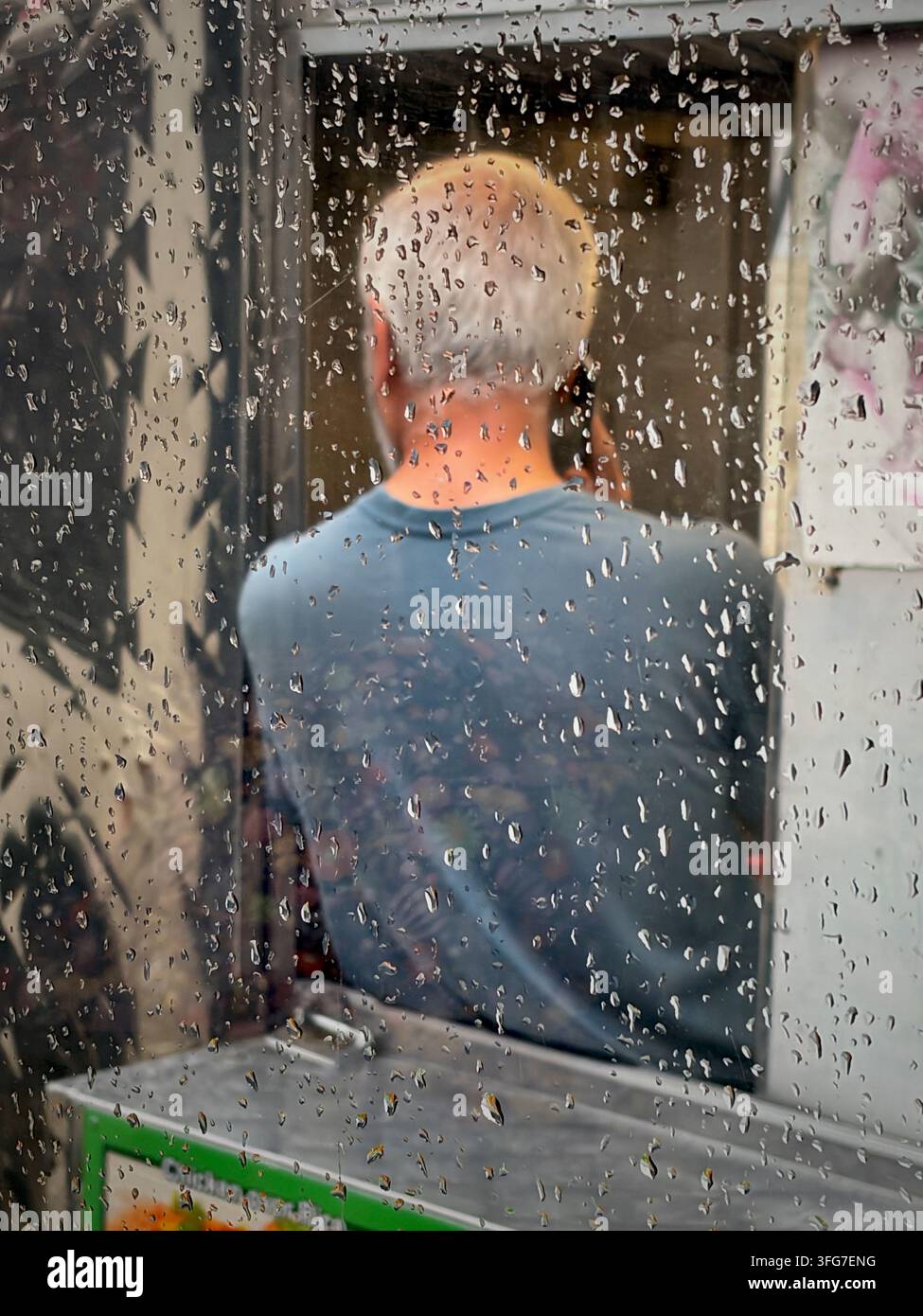 Philadelphia, PA, USA - 2. September 2026; Regentropfen auf einem Bus sind zu sehen, während ein Lebensmittelhändler ein Telefonat führt, während er sich durch das Fenster lehnt - Smartphone-aufgenommenes Stockfoto