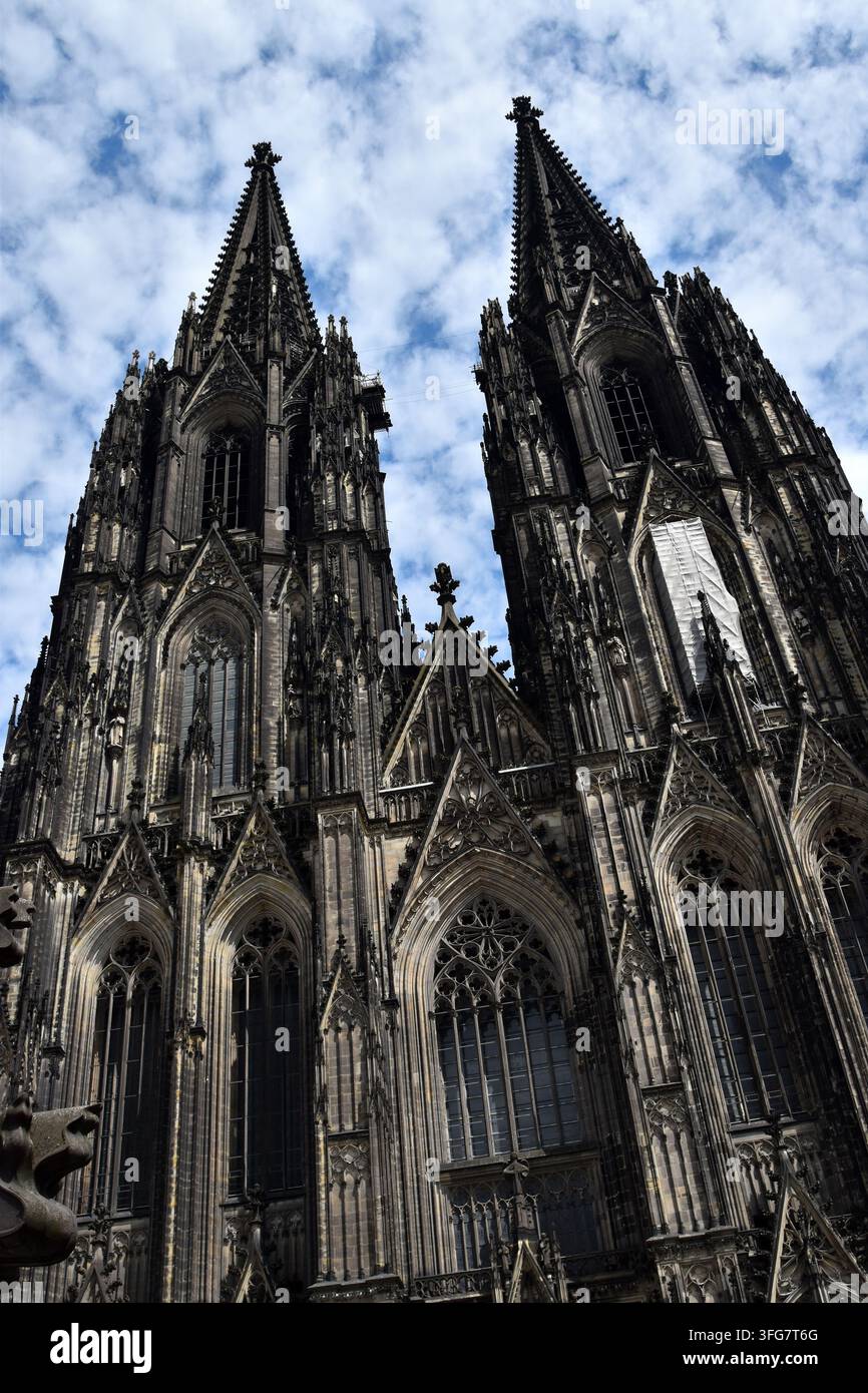 Die zwillingischen gotischen Türme des Kölner Doms vor einem gesprenkelten blauen bewölkten Himmel. Stockfoto