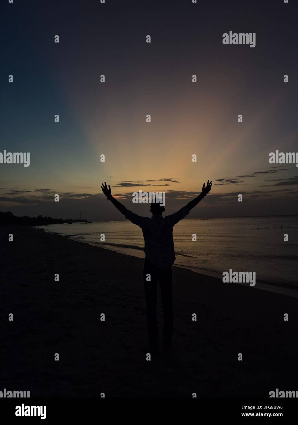 Silhouette einer Person mit erhobenen Armen bei Sonnenuntergang am Strand. - Smartphone-aufgenommenes Stockfoto