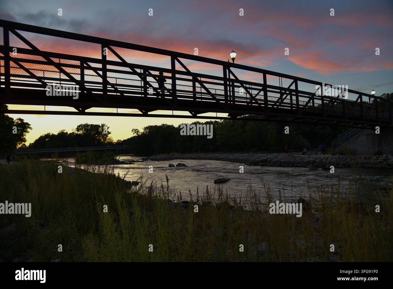 Fußgänger genießen das Abendrot von der Fußgängerbrücke über den Fox River in Yorkville, Illinois Stockfoto