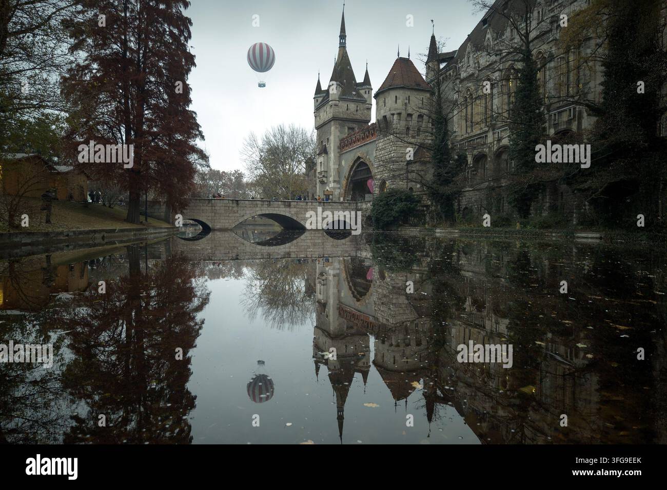 Heißluftballon fliegt über Burg Vajdahunyad mit Spiegelung im Seewasser im Budapester Stadtwald im Herbst Stockfoto