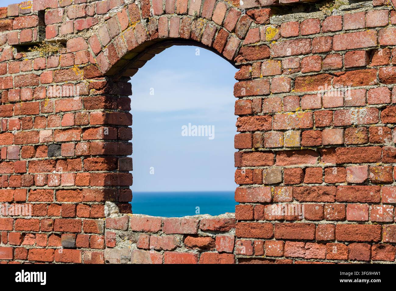 Gewölbte Öffnung in einer verfallenen Ziegelmauer mit Blick auf das offene Meer, Nahaufnahme von alten roten Ziegeln und Mörtel an einer Küsten-Erbestätte Stockfoto