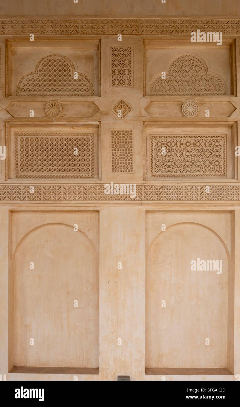 Komplexe geschnitzte geometrische Stuckreliefs und gewölbte Nischen schmücken eine traditionelle qatarische Lehmziegelgebäudewand in Al Khor, Katar. Stockfoto