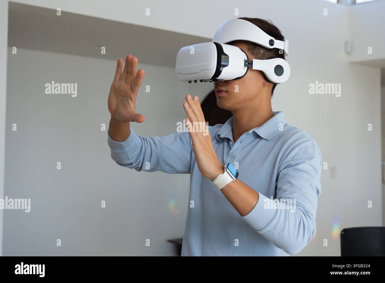 Asiatischer Mann trägt VR-Headset, Smartwatch, blaues Polohemd, nutzt virtuelle Anzeige in hellem Raum Stockfoto