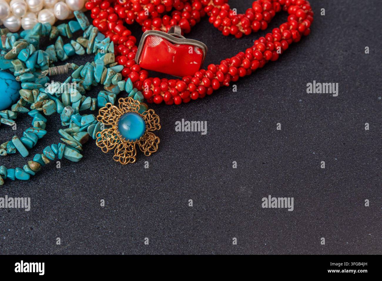Blaue, türkise und rote Korallen. Perlenhalsketten und goldene Broschen-Schmuck auf schwarzem Hintergrund. Stockfoto