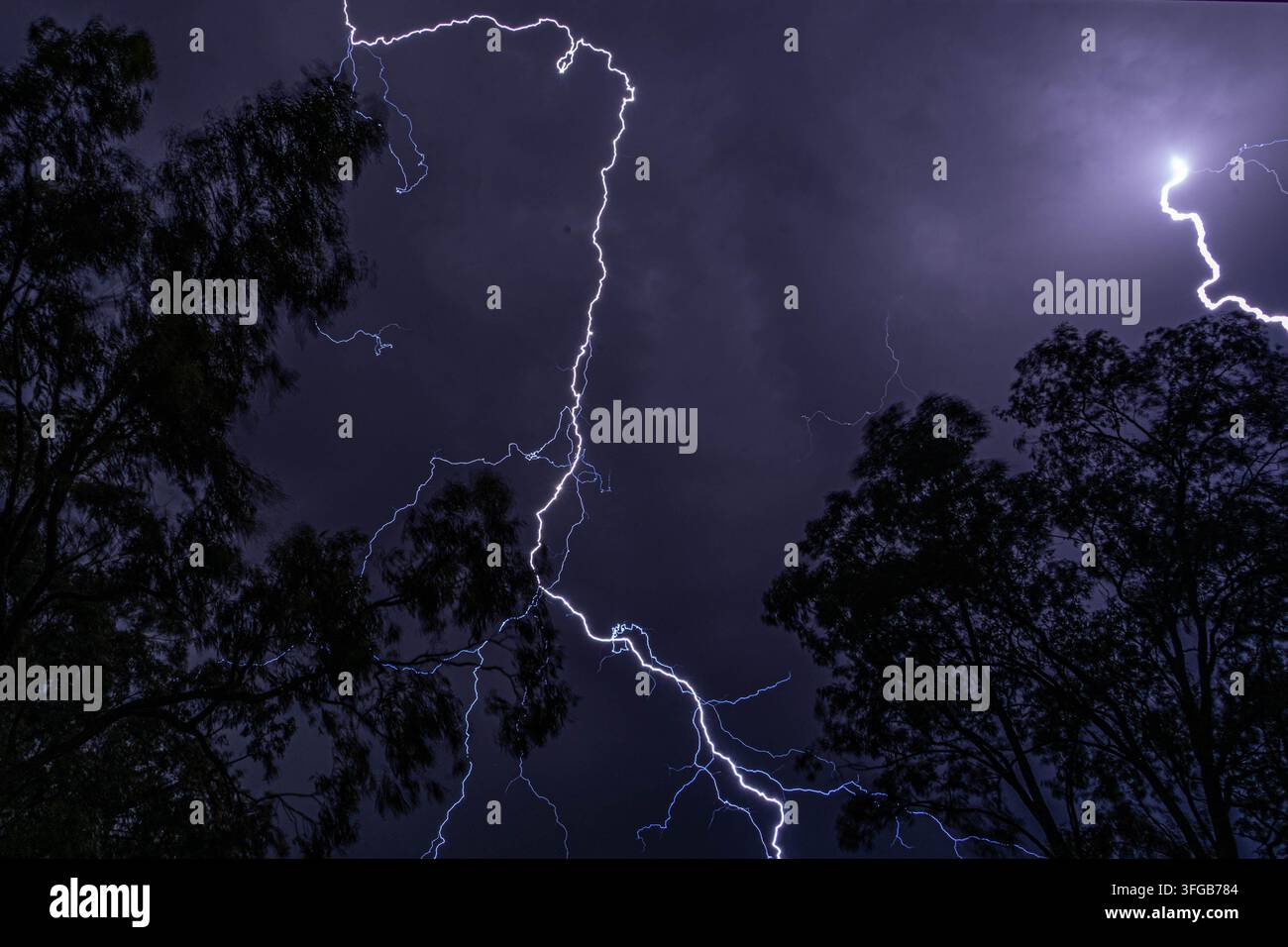 Dramatischer Gewittersturm mit kräftigen Blitzen, die die Stadt Skyline und dunkle stürmische Nachtwolken darüber beleuchten. Stockfoto