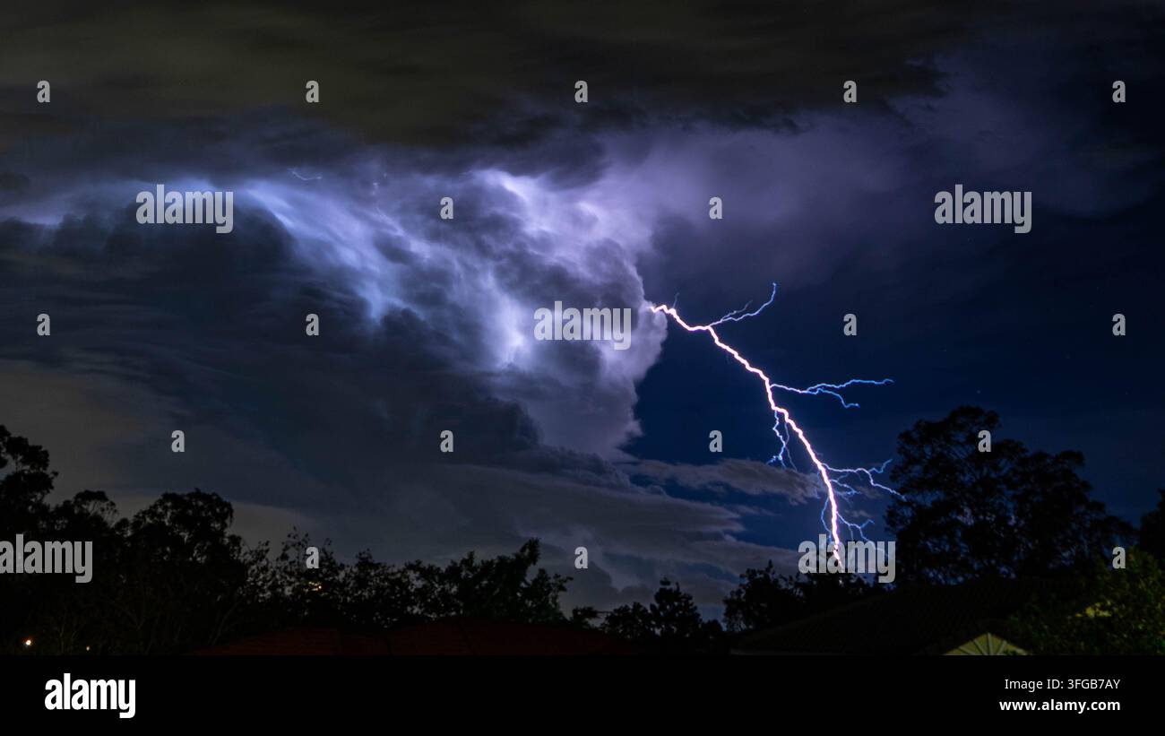 Dramatischer Gewittersturm mit kräftigen Blitzen, die die Stadt Skyline und dunkle stürmische Nachtwolken darüber beleuchten. Stockfoto
