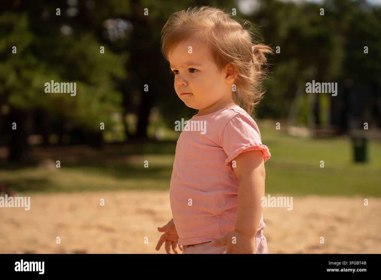 intimes Outdoor-Porträt einer blonden Frau in einer weichrosa Bluse, warm vom Sonnenlicht beleuchtet, mit zarten Haarsträhnen, einem friedlichen Ausdruck Stockfoto