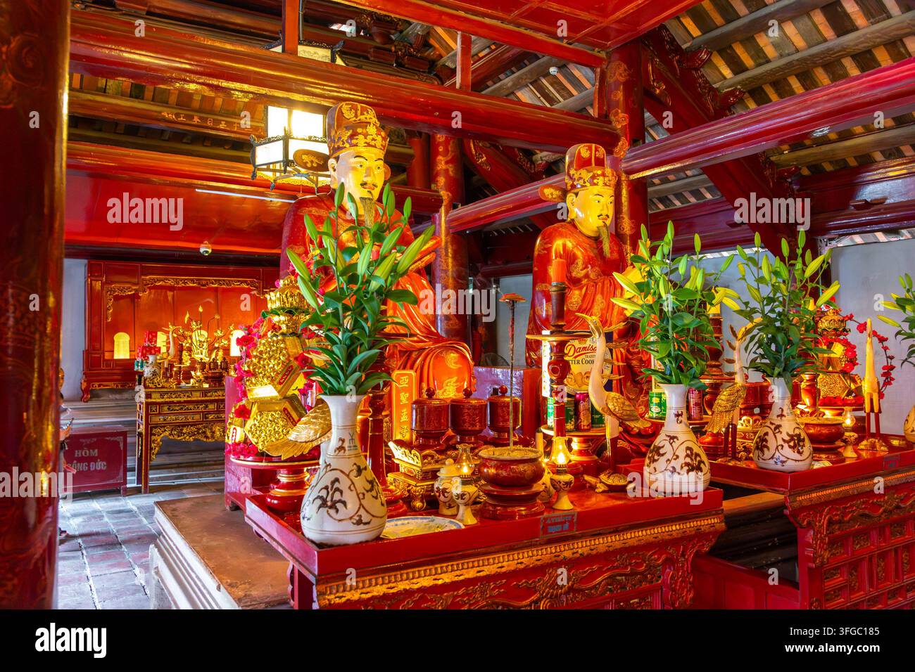 Hanoi, Vietnam - 22. Oktober 2023: Statuen von Gelehrten, die auf einem Altar sitzen, mit Opfergaben und roten Holzkonstruktionen Stockfoto
