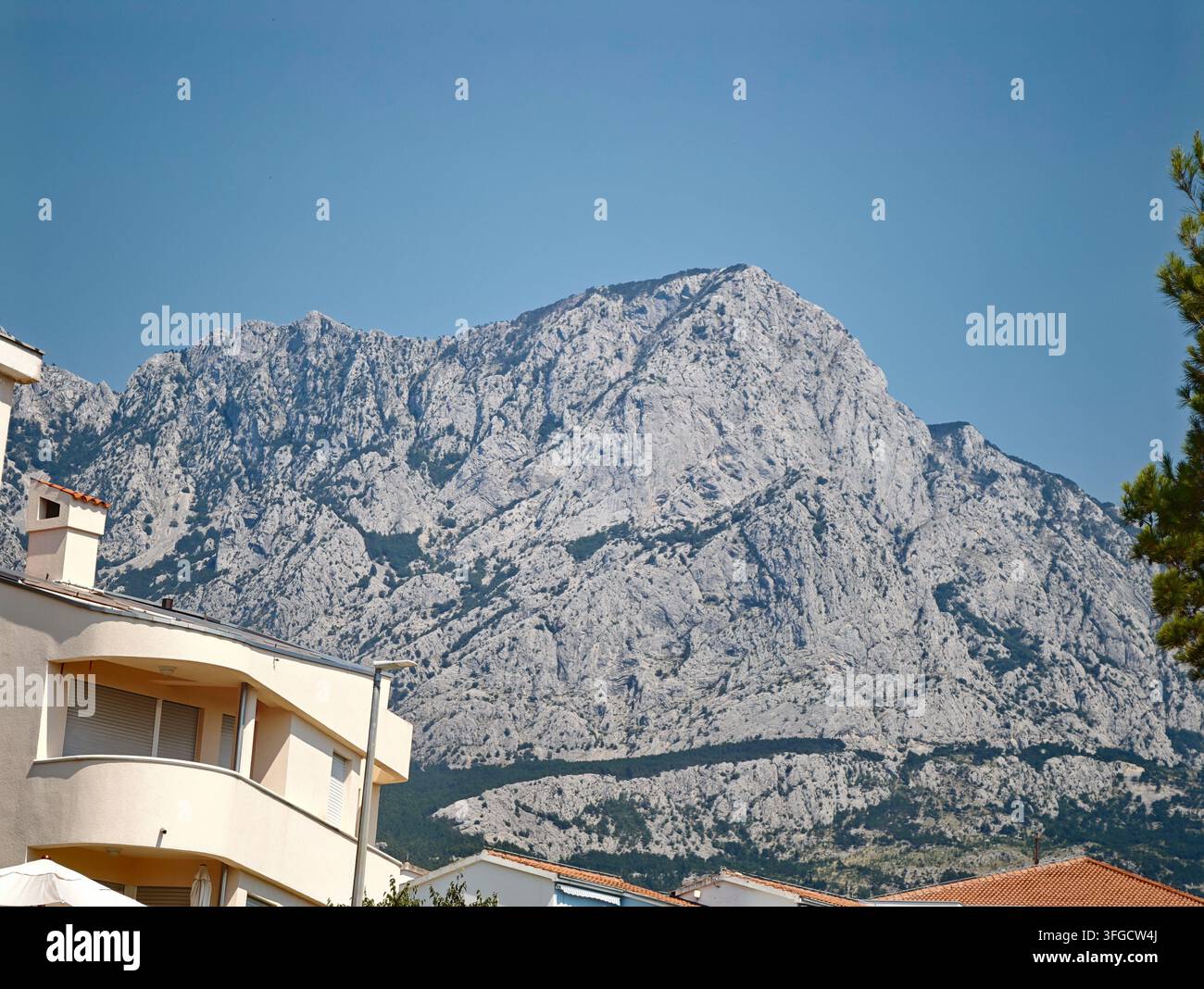 Ein atemberaubender Blick auf den massiven Biokovo-Berg, der majestätisch hinter sonnigen Wohnhäusern an der Küste von Baska Voda aufragt. - Smartphone-aufgenommenes Stockfoto