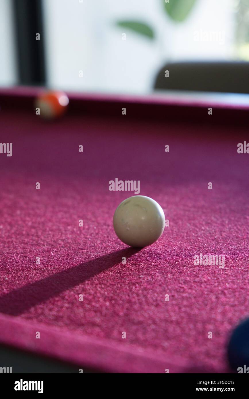 Weißer Spielball ruht auf rotem Filztisch und wirft einen langen Schatten nach links unten Stockfoto