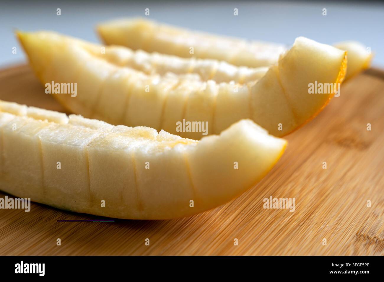 Drei frisch geschnittene Scheiben saftiger gelber Melone auf einem runden Holzschneidebrett. Stockfoto