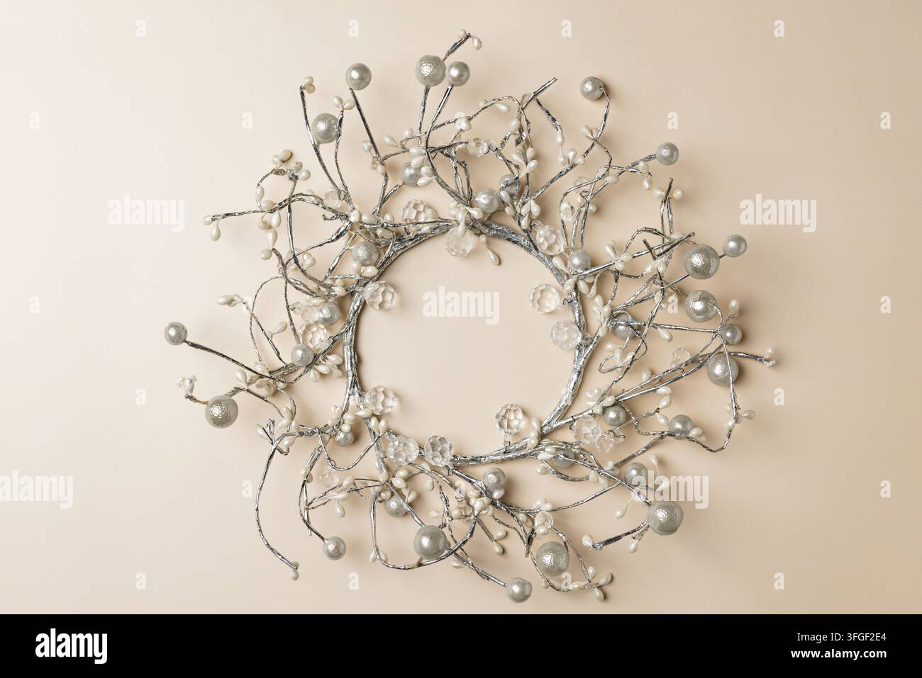 Zentrierter silberner Weihnachtskranz mit metallischen Beeren auf beigem Hintergrund für Neujahrskarten oder elegantes Winterfeiertagsdesign Stockfoto