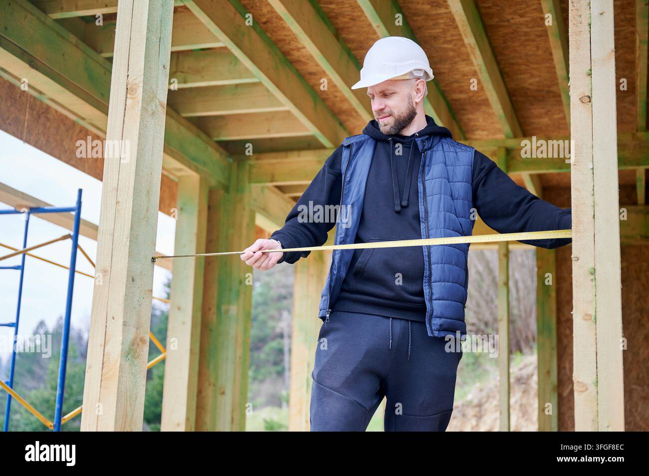 Bauprofi bewertet Abmessungen einer Holzkonstruktion, misst die Innenbreite und stellt sicher, dass Rahmen Elemente korrekt installiert sind Stockfoto