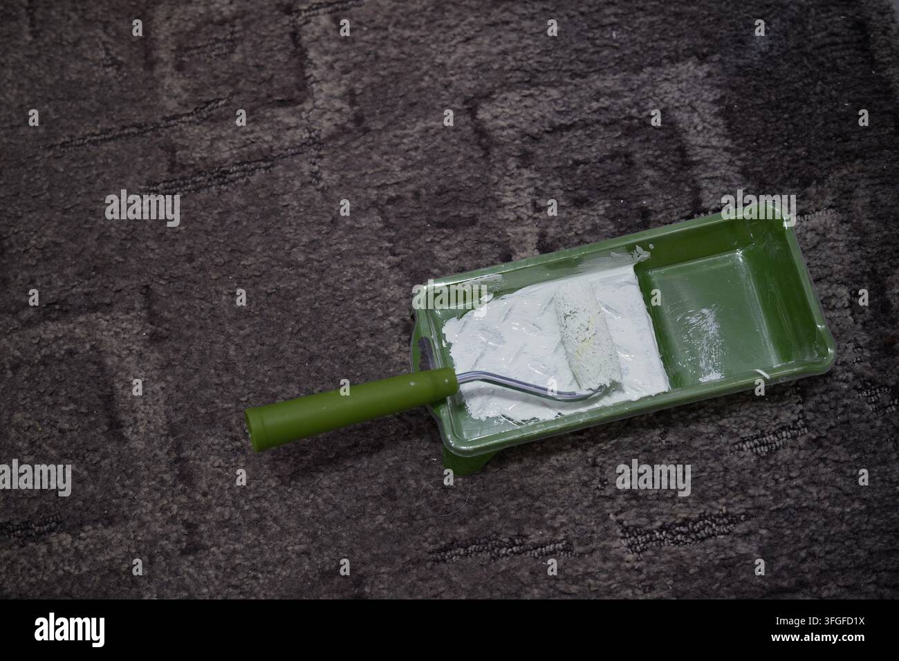 Nahaufnahme eines Mini-Farbtrollers in einer Schale mit hellgrüner Farbe. In einem hellen Raum während einer privaten Heimwerker-Renovierung. Stockfoto