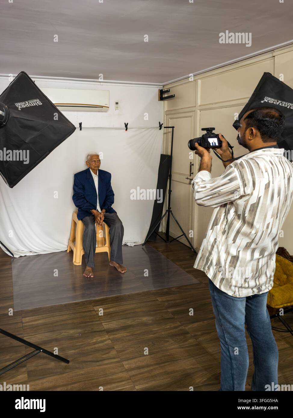 Ein Fotograf macht ein Porträt eines älteren Mannes in einer professionellen Studio-Umgebung in Gujarat, Indien. Die Szene zeigt Beleuchtungsausrüstung und ein Weiß - Smartphone-aufgenommenes Stockfoto
