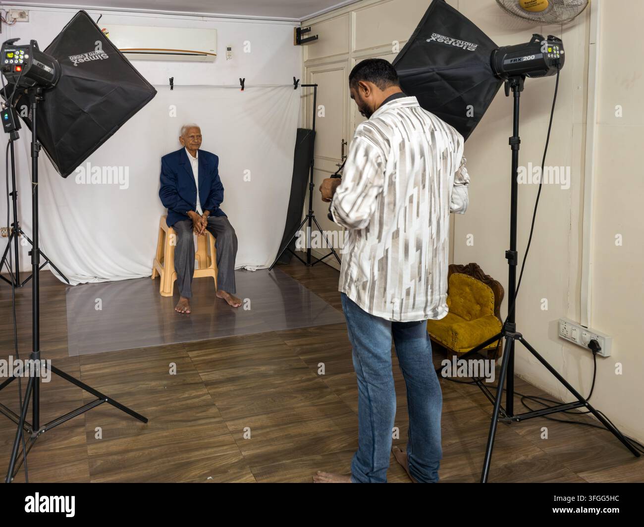 Ein Fotograf macht ein Porträt eines älteren Mannes in einer professionellen Studio-Umgebung in Gujarat, Indien. Die Szene zeigt Beleuchtungsausrüstung und ein Weiß - Smartphone-aufgenommenes Stockfoto