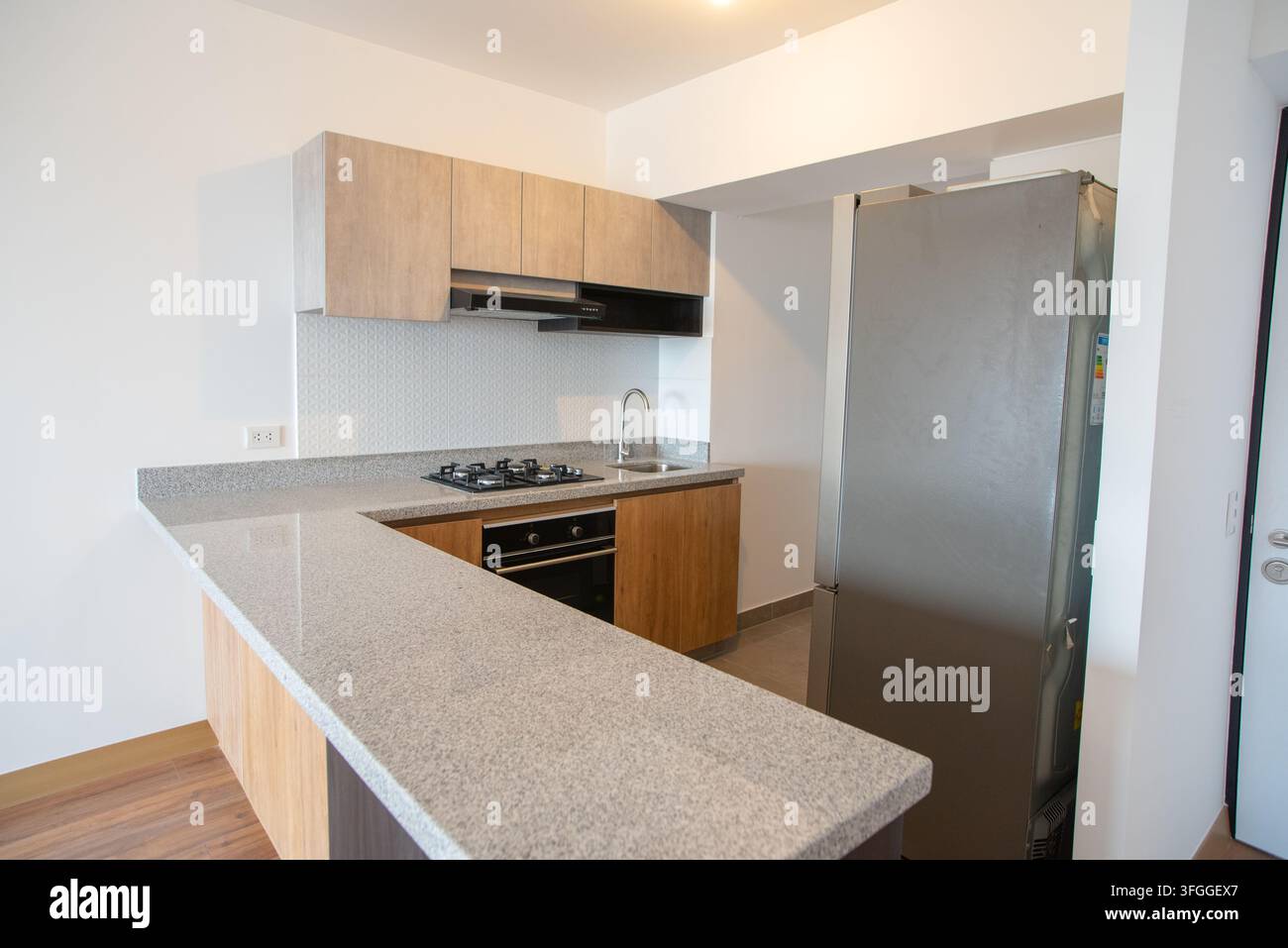 Moderne Kücheninsel: Eine schlanke, zeitgenössische Küche verfügt über eine Insel mit Granitoberfläche und einer Frühstücksbar sowie moderne Schränke Stockfoto