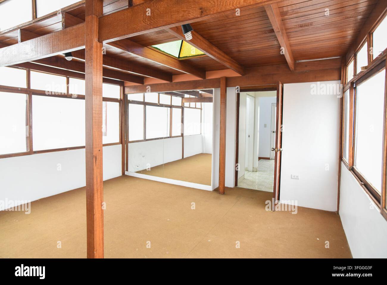 Interieur eines Loftraums mit Holzträgern und Teppichboden: Ein geräumiger Loftbereich mit freiliegenden Holzträgern, einem Teppichboden und einem großen Fenster Stockfoto