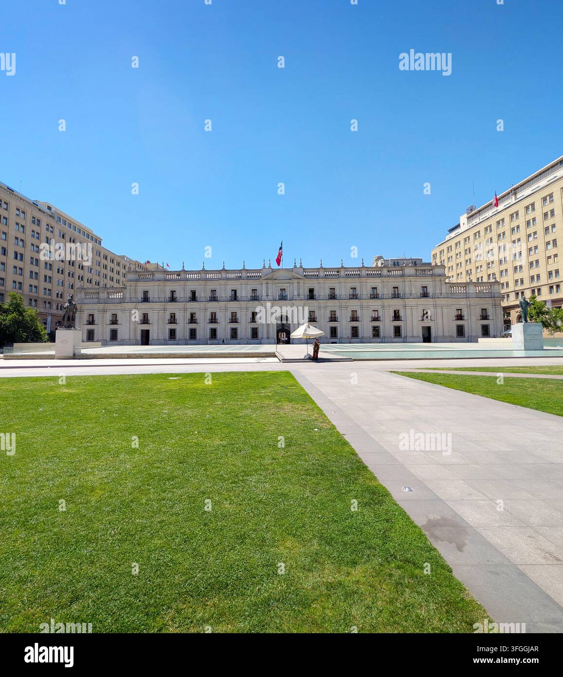 SANTIAGO, CHILE - 03. DEZEMBER 2025: Die große Fassade des La-Moneda-Palastes erhebt sich hinter einem grasbewachsenen Platz an der Plaza de la Ciudadania unter einem klaren blauen Himmel in Stockfoto