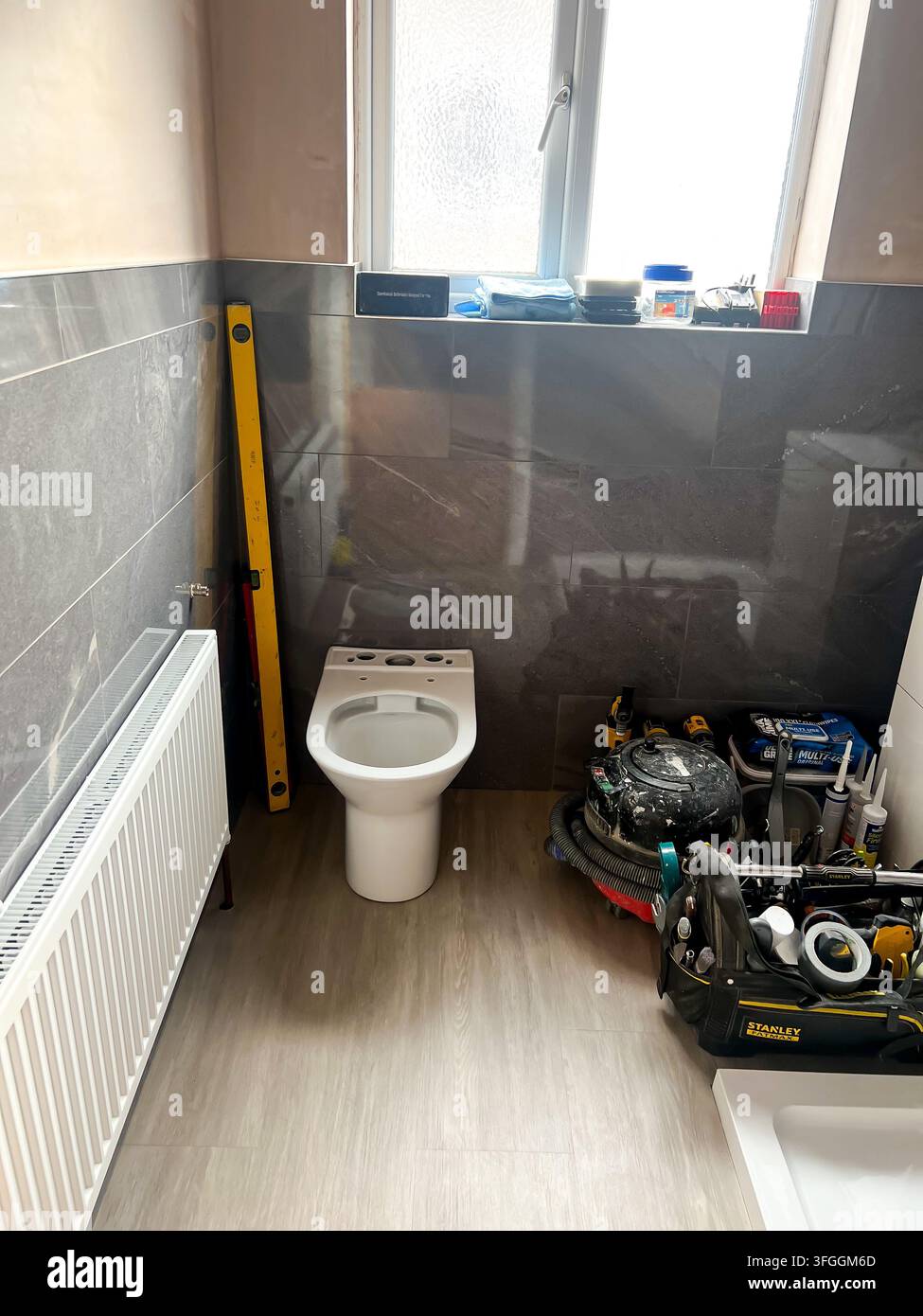 Ein Badezimmer mitten in der Renovierung mit neu gefliesten Wänden, neuem Bodenbelag und einer teilweise montierten Toilette - Smartphone-aufgenommenes Stockfoto