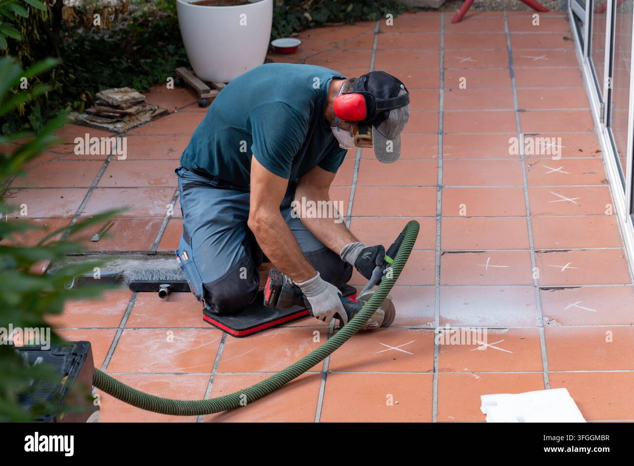 Ein Arbeiter schleift Terracottafliesen auf einer Außenterrasse mit Elektrowerkzeugen. Stockfoto