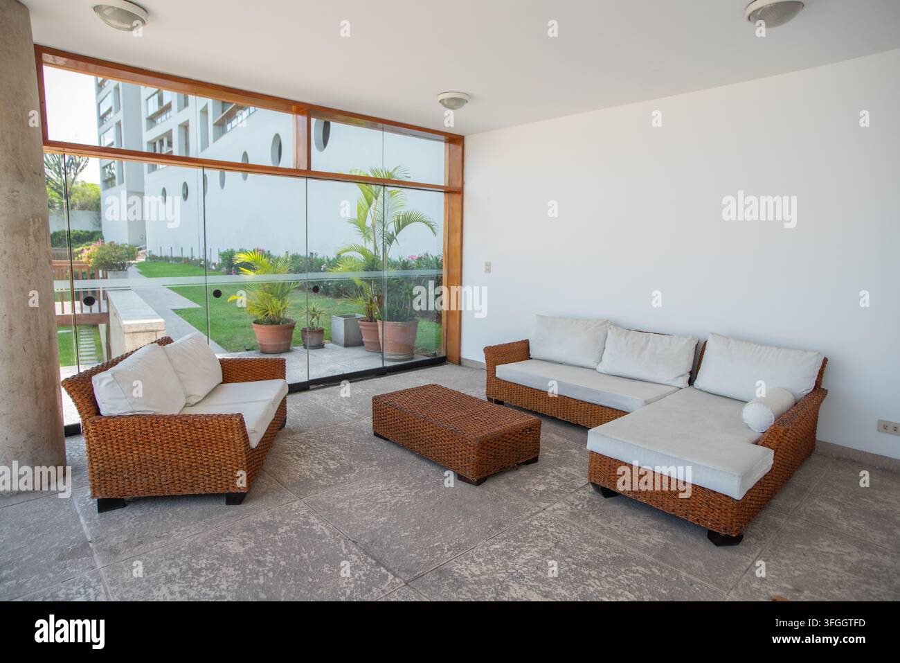 Moderner Wohnraum: Ein zeitgenössisches Wohnzimmer, ausgestattet mit einem Schlafsofa, einem Zweisitzsofa und einem Korbhocker, mit Blick auf eine ruhige Gartenterrasse Stockfoto