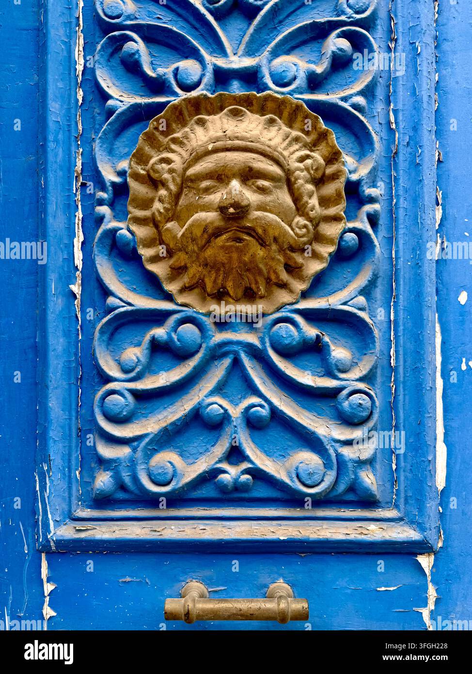 Verzierte blau lackierte Türdetails mit einer geschnitzten bärtigen Maske und dekorativer Schnörkelarbeit in Tunis, Tunesien - Smartphone-aufgenommenes Stockfoto