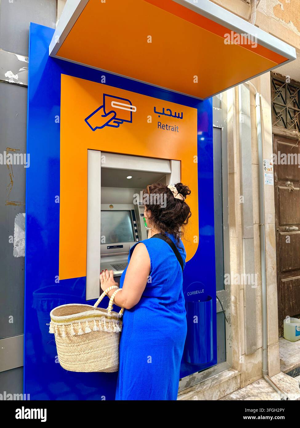 Frau, die Bargeld von einem Geldautomaten in der Medina von Sousse, Tunesien, abhebt, was den Zugang zu Finanzen, modernes Bankwesen und das zeitgenössische Wirtschaftsleben veranschaulicht - Smartphone-aufgenommenes Stockfoto