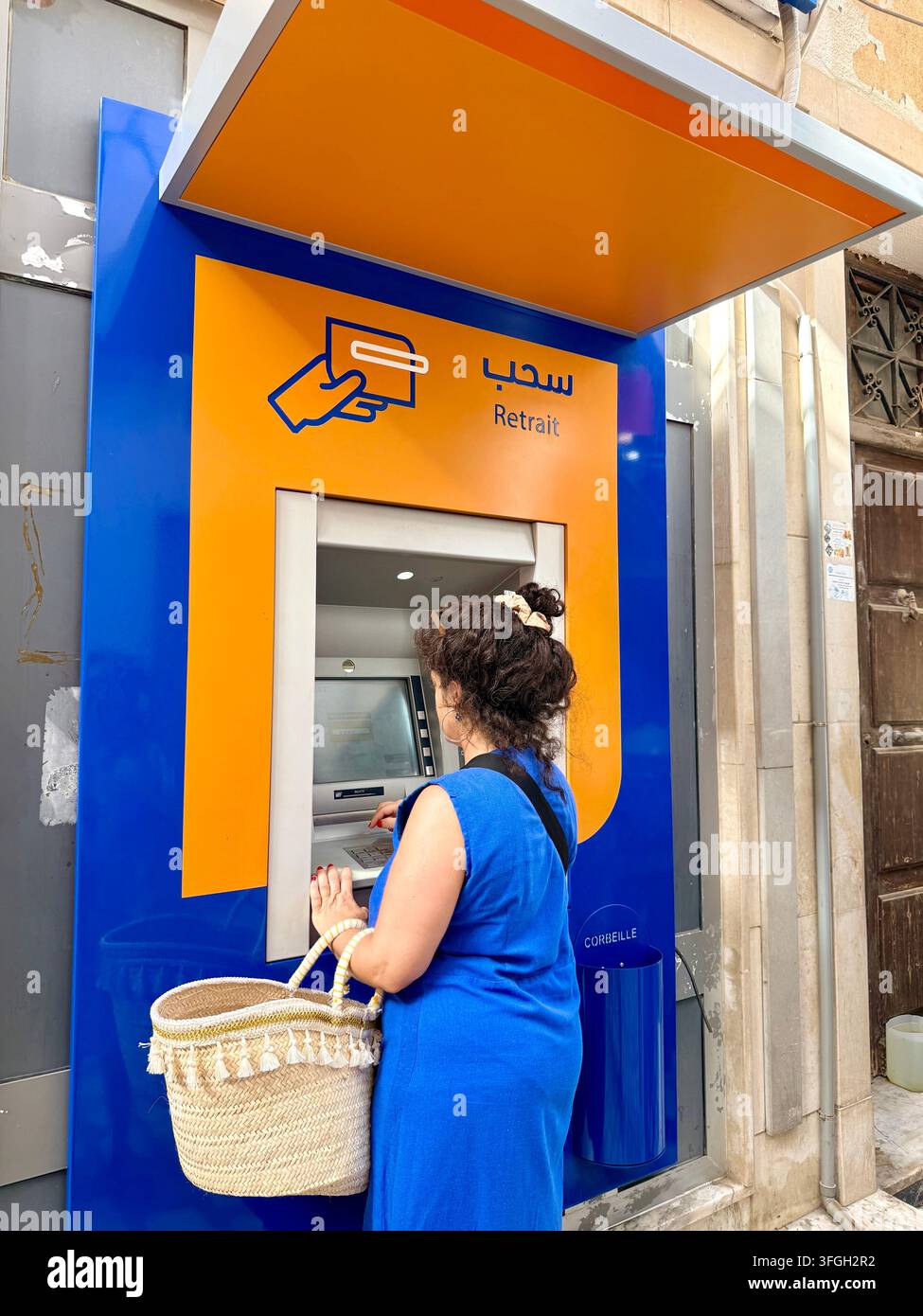 Frau, die Bargeld von einem Geldautomaten in der Medina von Sousse, Tunesien, abhebt, was den Zugang zu Finanzen, modernes Bankwesen und das zeitgenössische Wirtschaftsleben veranschaulicht - Smartphone-aufgenommenes Stockfoto