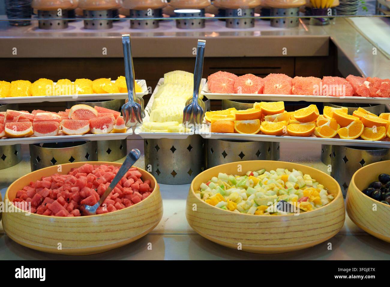 Eine breite Auswahl an frischen Früchten auf einem Hotel-Frühstücksbuffet mit geschnittenen Orangen, Grapefruits, Melone, gewürfelter Wassermelone in Holzschüsseln und Obst Stockfoto