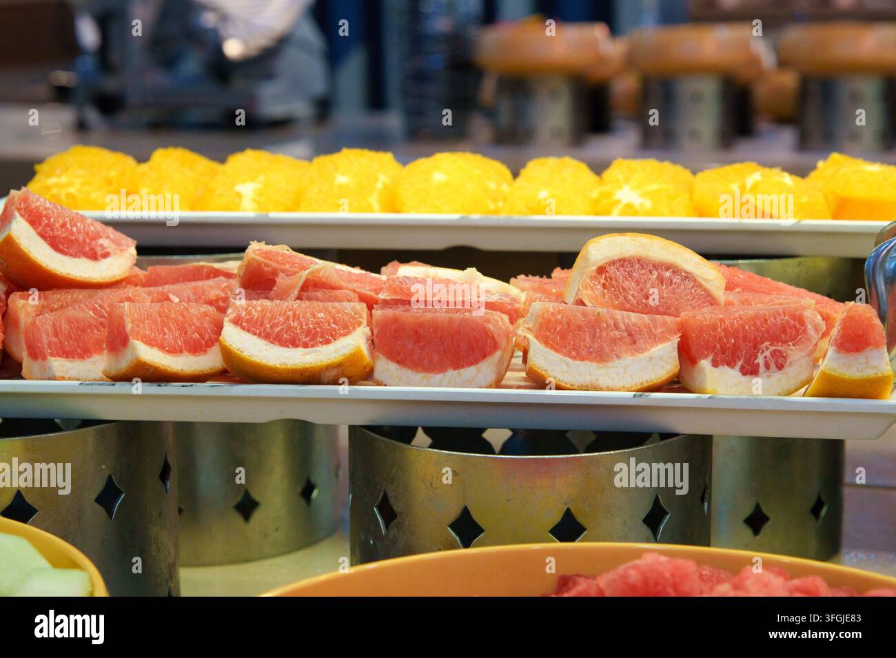 Eine Auswahl an frisch geschnittenen rosa Grapefruit-Keilen und saftigen Orangenscheiben, die auf weißen Tabletts an einem Hotel-Frühstücksbuffet arrangiert sind. Hervorhebung von gesundem Fo Stockfoto