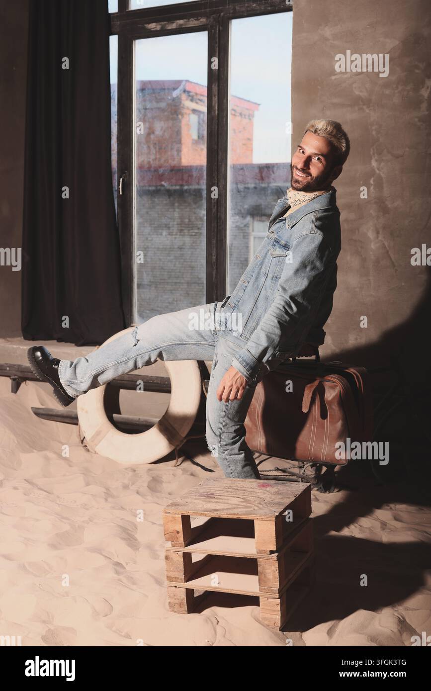 Blondhaarige Darstellerin steht mit Mantel in der Nähe eines hellen Fensters Stockfoto