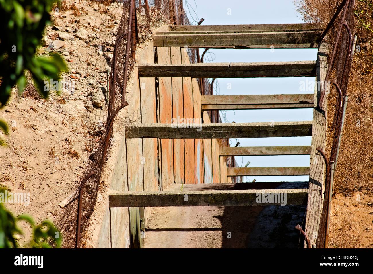 Verwitterte Betonträger überspannen einen schmalen Kanal neben trockenen Hängen und Zäunen an einem landwirtschaftlichen Standort in Riverside, Kalifornien. Stockfoto