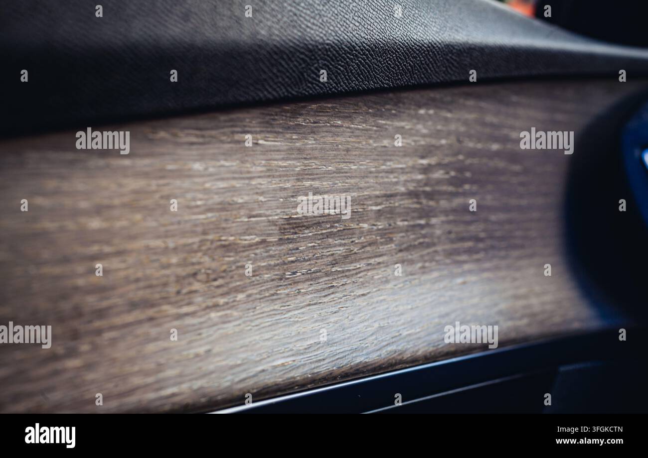 Nahaufnahme des Interieurs eines modernen Luxusautos mit einer Türverkleidung aus texturiertem Naturholz mit offenporiger Holzmaserung und dunklem Leder. Stockfoto