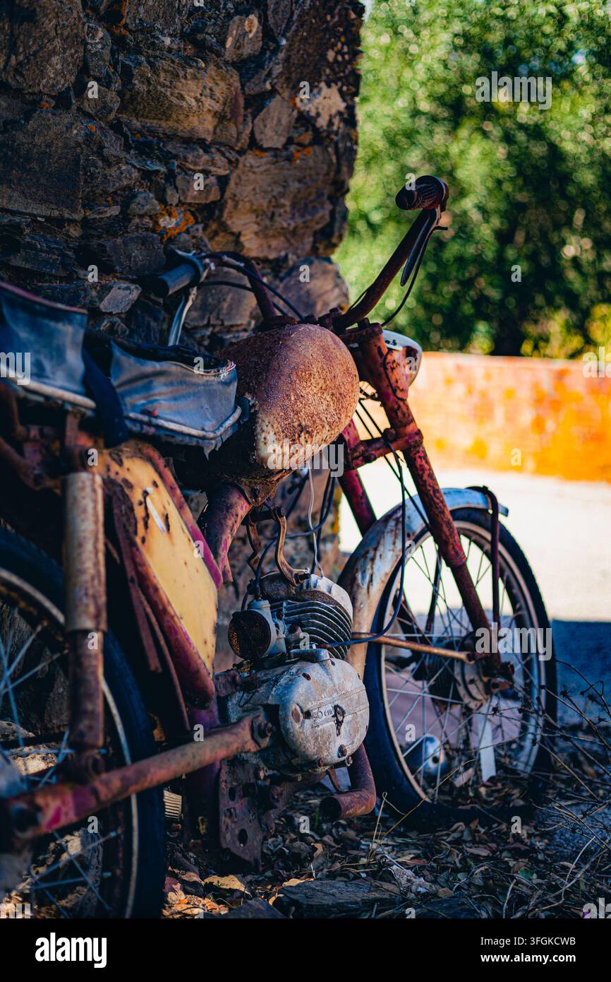 Altes, verrostetes Vintage-Moped, das an einer rustikalen Steinmauer im Freien in einer ländlichen Dorfkulisse in Portugal geparkt ist. Stockfoto